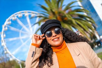 Woman with hat and sunglasses visiting a city with a ferris wheel in winter