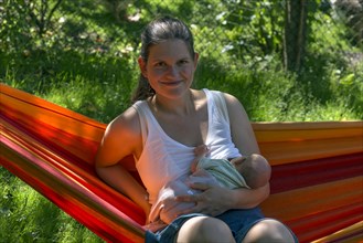 Young mother with baby in a hammock in the garden