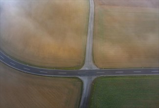 Drone view of a rural landscape shrouded in dense morning fog with a road junction near Prambachkirchen