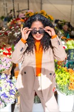 Vertical portrait of a cute latin woman holding her sunglasses in a floral market in a sunny day of autumn