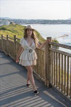 Vertical photo of a chic blonde woman walking along a promenade with sea views