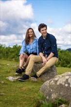 Vertical photo of a young couple sitting on a rock in the mountain
