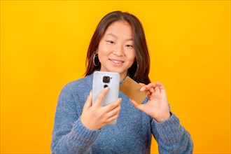 Studio photo with yellow background of a chinese woman using mobile and card to shopping online
