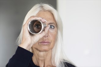 Elderly woman with long hair looking through a metal pipe at work