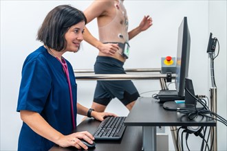 Patient walking along a treadmill performing a cardiovascular stress test while a cardiologist female doctor monitoring it