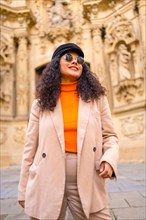 Stylish latin woman standing with warm elegant clothes in a square with an ancient monument