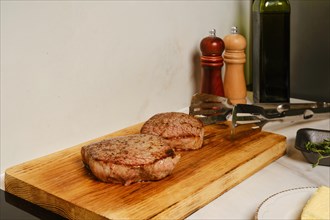 Two pieces of fried beef steak rest on wooden cutting board