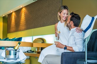 Couple drinking champagne in a luxury hotel room sitting on sofa next to the luggage