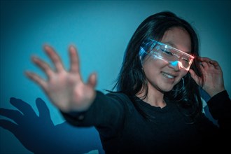 Studio photo with blue background with neon lights of a chinese woman gesturing having fun using an augmented reality goggles