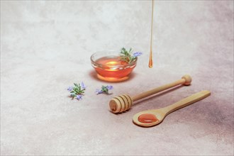 Natural honey dripping on a wooden spoon with rosemary blossom branches and a bowl with honey