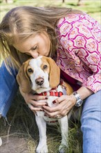 Blond mid adult woman kissing her Beagle dog while he is looking at camera at the park