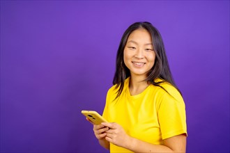 Studio photo with purple background of a chinese woman using phone and smiling at camera