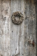 Very old weathered wooden door with a wreath of twigs and lichen