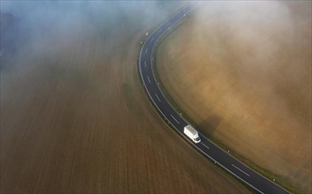 Drone view of a rural landscape shrouded in dense morning fog with a country road near Prambachkirchen