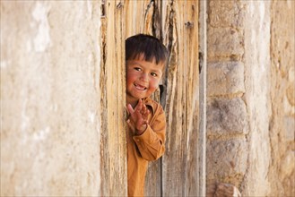Happy young Bolivian boy in doorway waving in the town Tarabuco