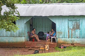 Family posing at wooden hut with corrugated sheet roof in rural village near Ciudad del Este