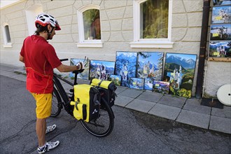 Cyclist looking at kitsch postcards and paintings in front of Hohenschwangau Castle