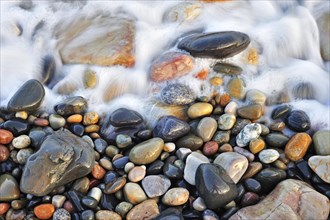Colourful water smoothed pebbles in surf at shingle beach