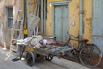 Old man sleeping on wooden cart in street in Old Delhi