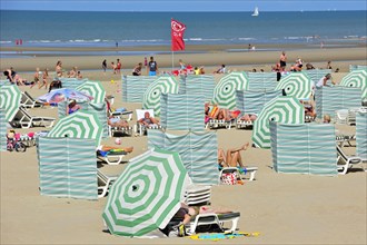Sunbathers in summer sunbathing behind parasols and windbreaks on beach along the North Sea coast at Koksijde