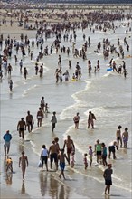 Tourists in swimsuits on crowded beach paddling in the North Sea on a hot day during the summer holidays