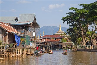 Intha villagers in proas at lakeside village with traditional bamboo houses on stilts and Buddhist temple