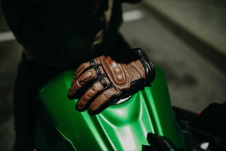 A brown leather motorcyclist glove lies on the tank of a green motorcycle