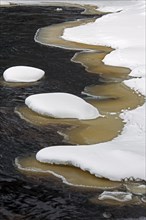 Brown slush ice along riverbank covered in snow in winter