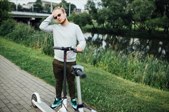 Young handsome blond man is waiting for a friend to go on a trip on electric scooters