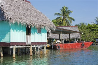 Red boat and wooden house on stilts with thatched roof on the Dulce River
