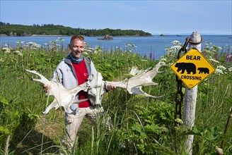 Tourist posing with moose antlers in front of Attention Bear sign in the garden of Katmai Wilderness Lodge