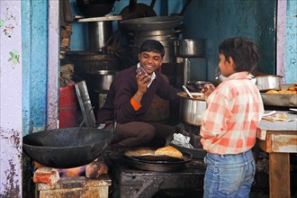 Boy preparing food while making a call with his cellular phone in Old Delhi