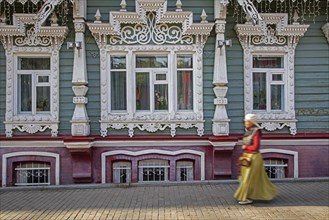 Russian woman walking in front of traditional ornate wooden house in the city Perm