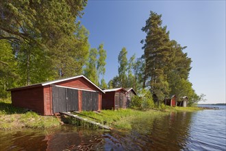 Red wooden boathouses along lake Siljan in summer
