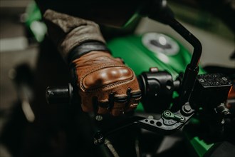A motorcyclist in brown leather gloves sits on a motorcycle