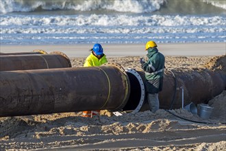 Dredging workers connecting pipes of pipeline during sand replenishment