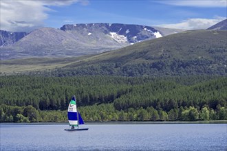 Sailing boat on Loch Morlich in front of the Cairngorm Mountains