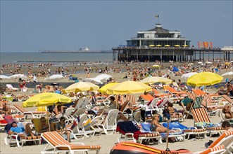Tourists sunbathing on the beach during the summer holidays and the pier at seaside resort Blankenberge