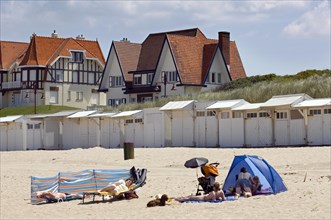 Tourists sunbathing in front of beach cabins and houses in Belle Epoque style of the consession at seaside resort De Haan