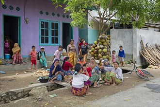 Indonesian women and children preparing food by squeezing coconut meat in village on the island Lombok
