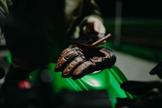 A brown leather motorcyclist glove lies on the tank of a green motorcycle