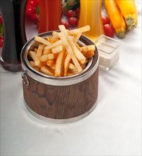 Fresh french fries on a wood bucket with selection of beers and fresh vegetables on background