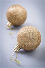 Two gold colored christmas balls on grey background