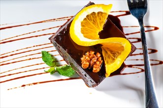 Fresh baked delicious chocolate and walnuts cake with slice of orance on top and mint leaf
