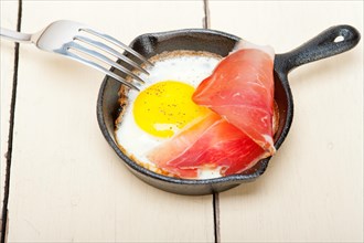 Fried egg sunny side up with Italian tyrolean speck smoked ham on a skillet
