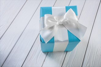 Blue gift box with white ribbon on a white wooden board