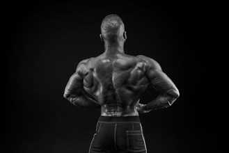 Silhouette of a strong bodybuilder. View from the back. Confident young fitness athlete with a powerful body and perfect abs. Black and white photography. Dramatic light