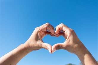 Woman's hands showing heart sign on blue sky background