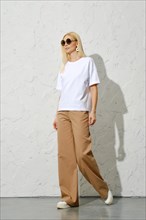 A fashionable adult woman in casual loose trousers and white shirt walks in the studio