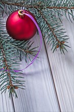 Matt red Christmas bauble and fir tree branch on white wooden panels